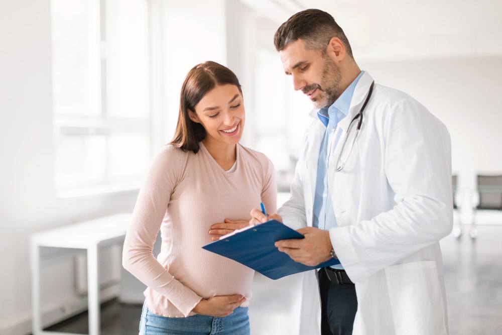 male-doctor-showing-clipboard-with-medical-test-results-happy-pregnant-lady-during-meeting-clinic (1)