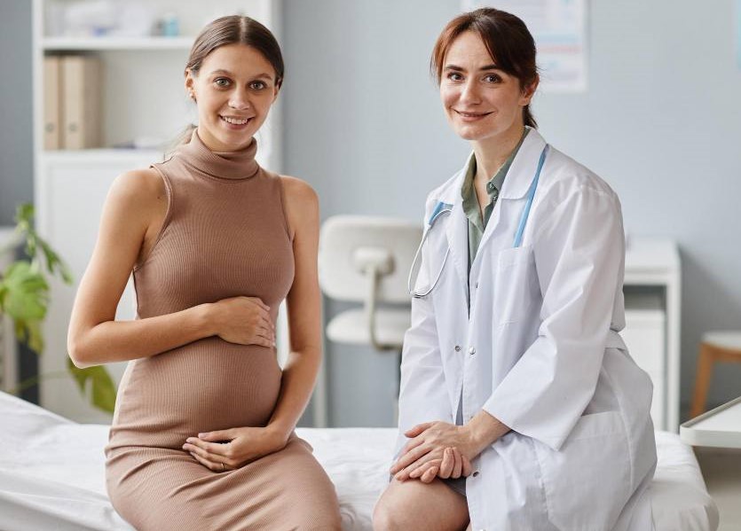 portrait-pregnant-woman-her-gynecologist-smiling-camera-together-while-sitting-couch-doctors-office